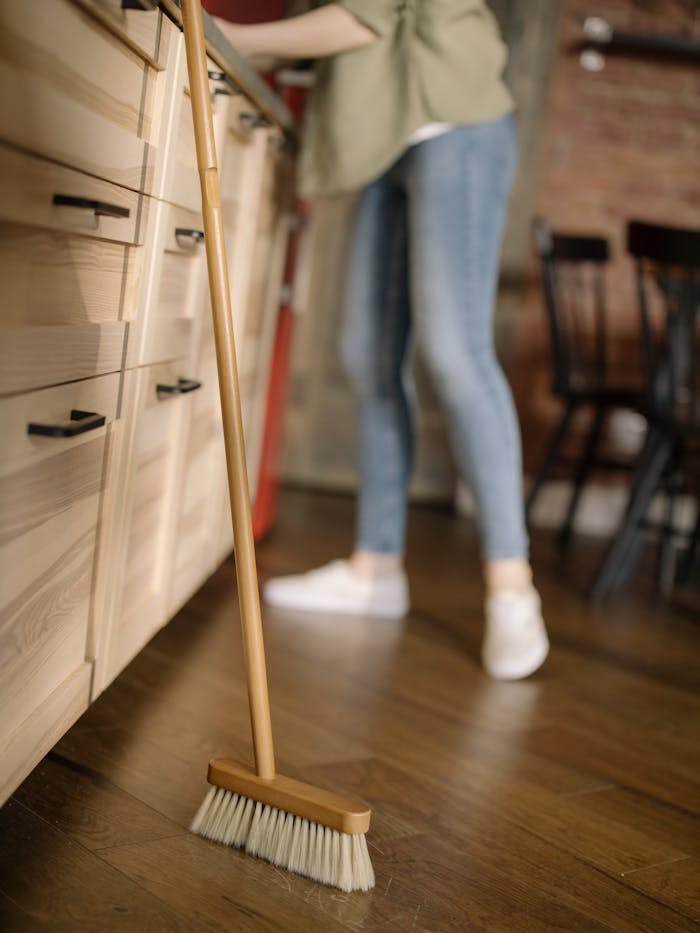services-02 A woman in casual attire sweeps the kitchen floor, maintaining cleanliness in a cozy home.