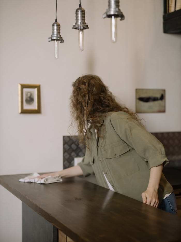 services-01 A woman with curly hair wipes a kitchen counter in a beautifully decorated home interior.
