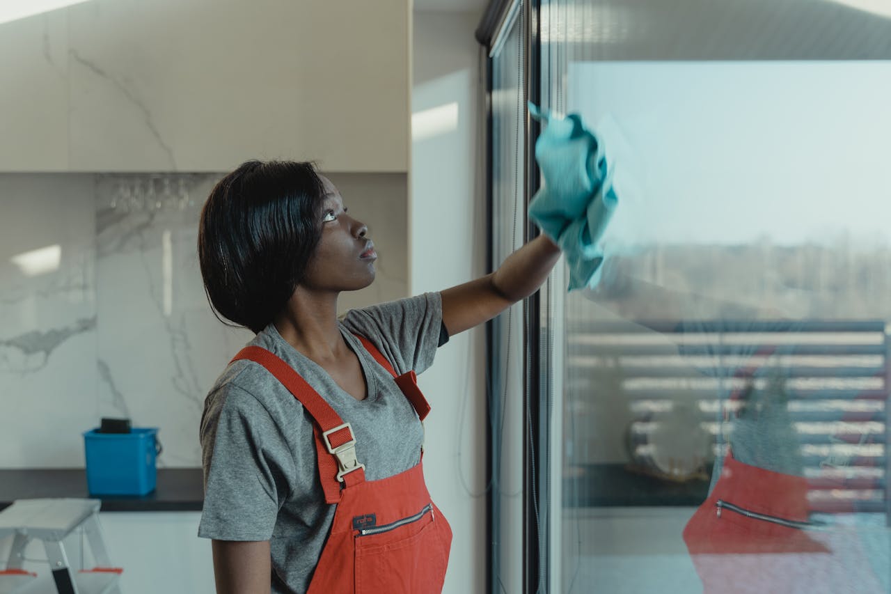 our-story A woman in overalls cleans a glass window with a rag, emphasizing professional housekeeping.