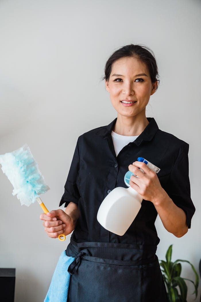 about-us A female housekeeper smiling while holding cleaning tools indoor.